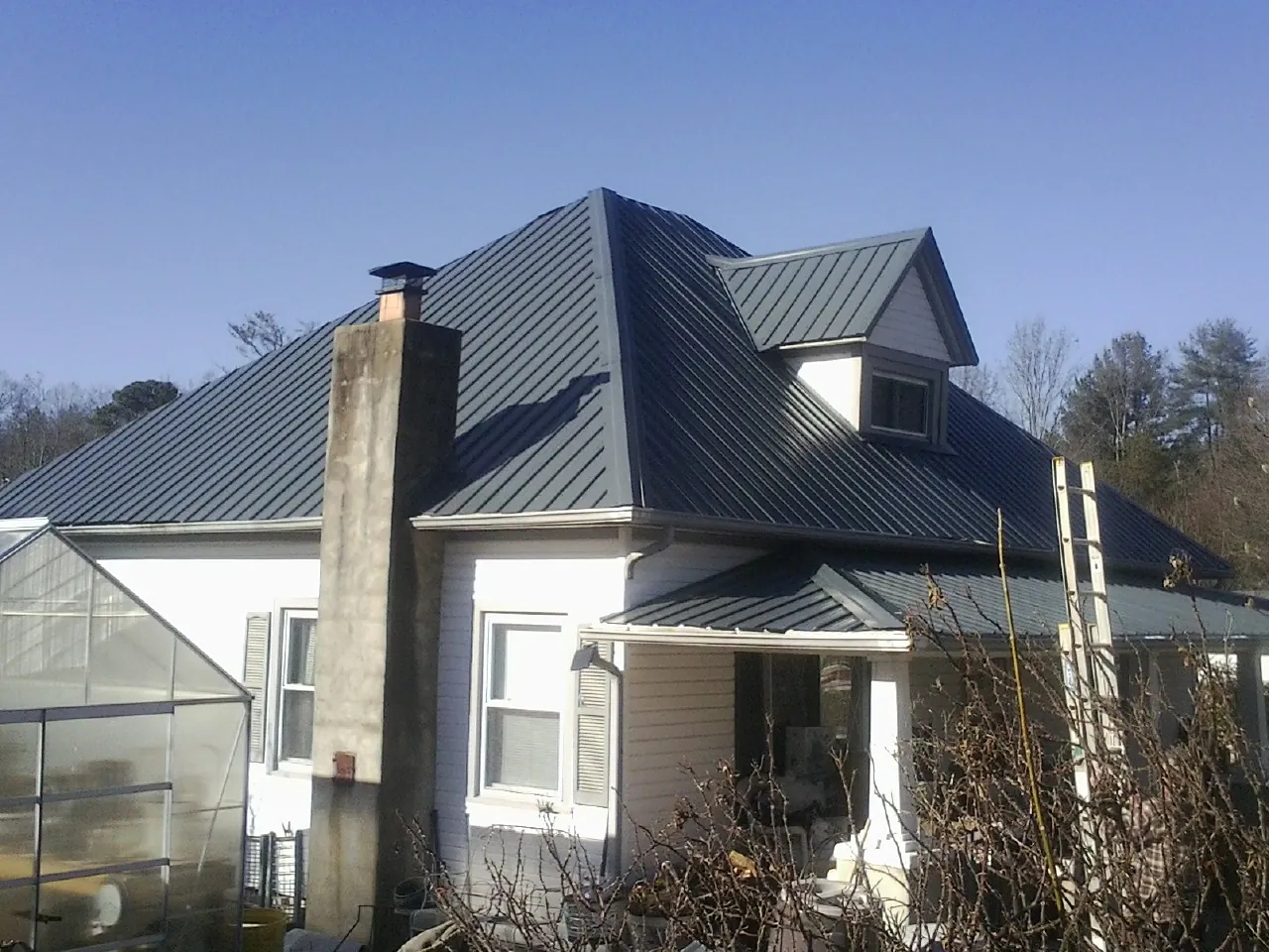 Dark blue standing seam metal roof on a white farmhouse with dormer — Slate & Tile Roof Repair by Roofing Brothers in Pottersdale