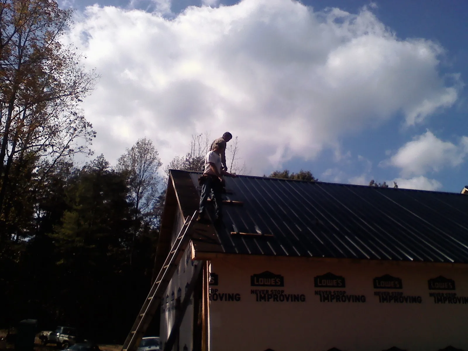 Roofer fastening dark metal panels high against a cloudy sky, from a Roof Inspection job in Pottersdale