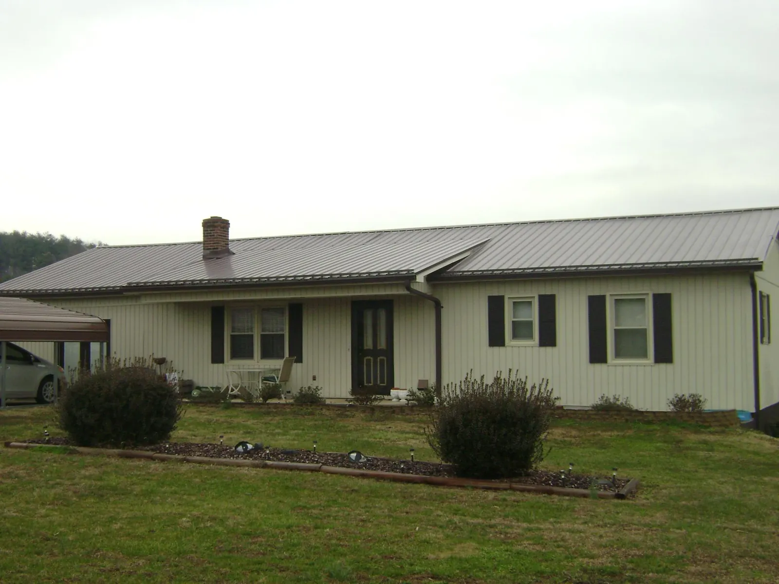 Brown metal roof on a cream sided ranch home with a brick chimney in Pottersdale