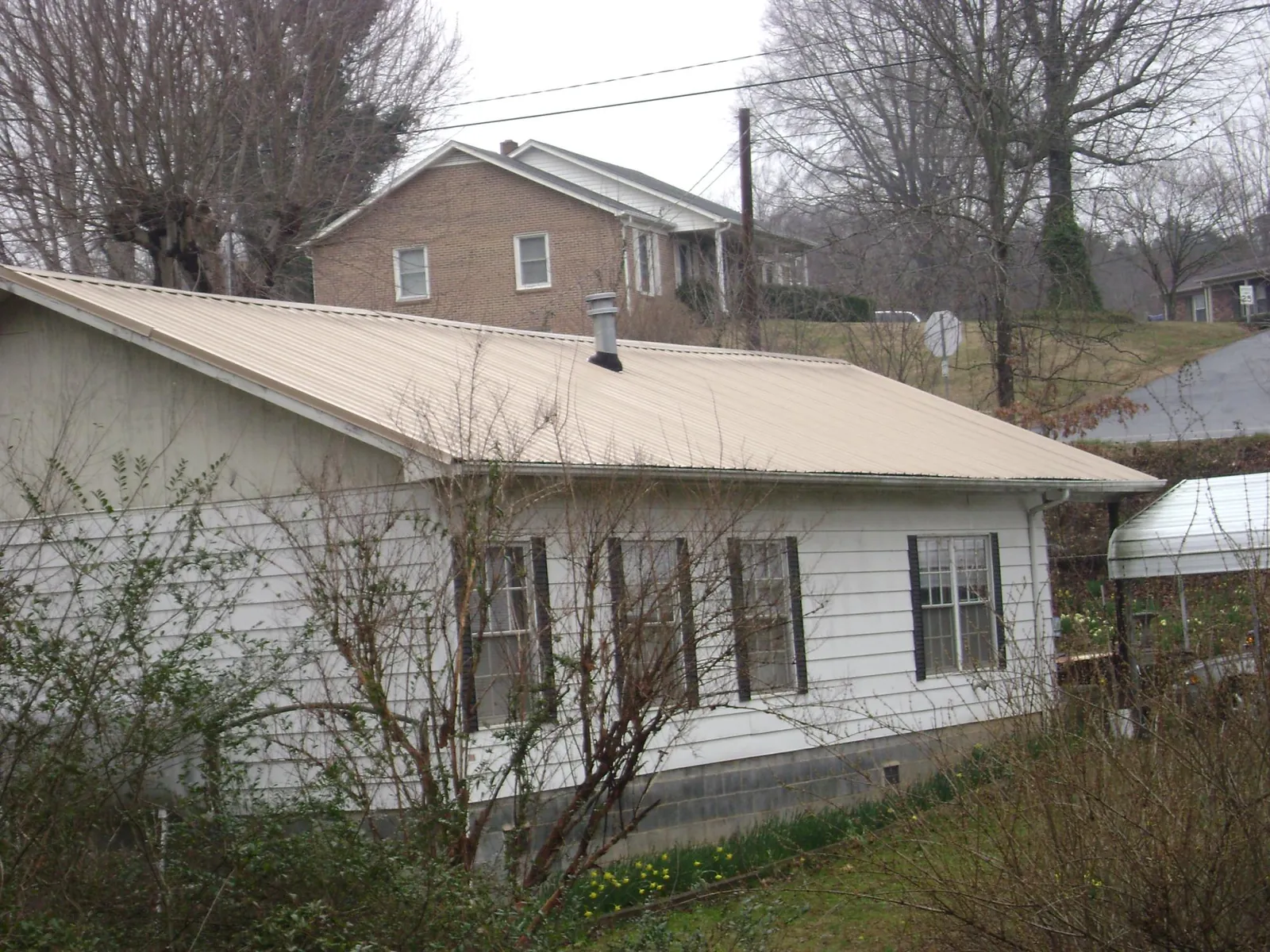 Tan metal roof on a white sided house set into a hillside — Commercial Roofing by Roofing Brothers in Pottersdale
